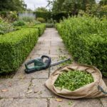 Hedgerow hedge trimmer beside a half-trimmed hedge and a tarp of clippings