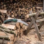 Sawtooth folding pruning saw on a woodpile beside cut branches and a sawhorse