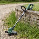 Trailhead 40V cordless string trimmer leaning against a low stone garden wall