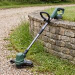 Trailhead string trimmer beside a crisply trimmed lawn edge on a gravel driveway